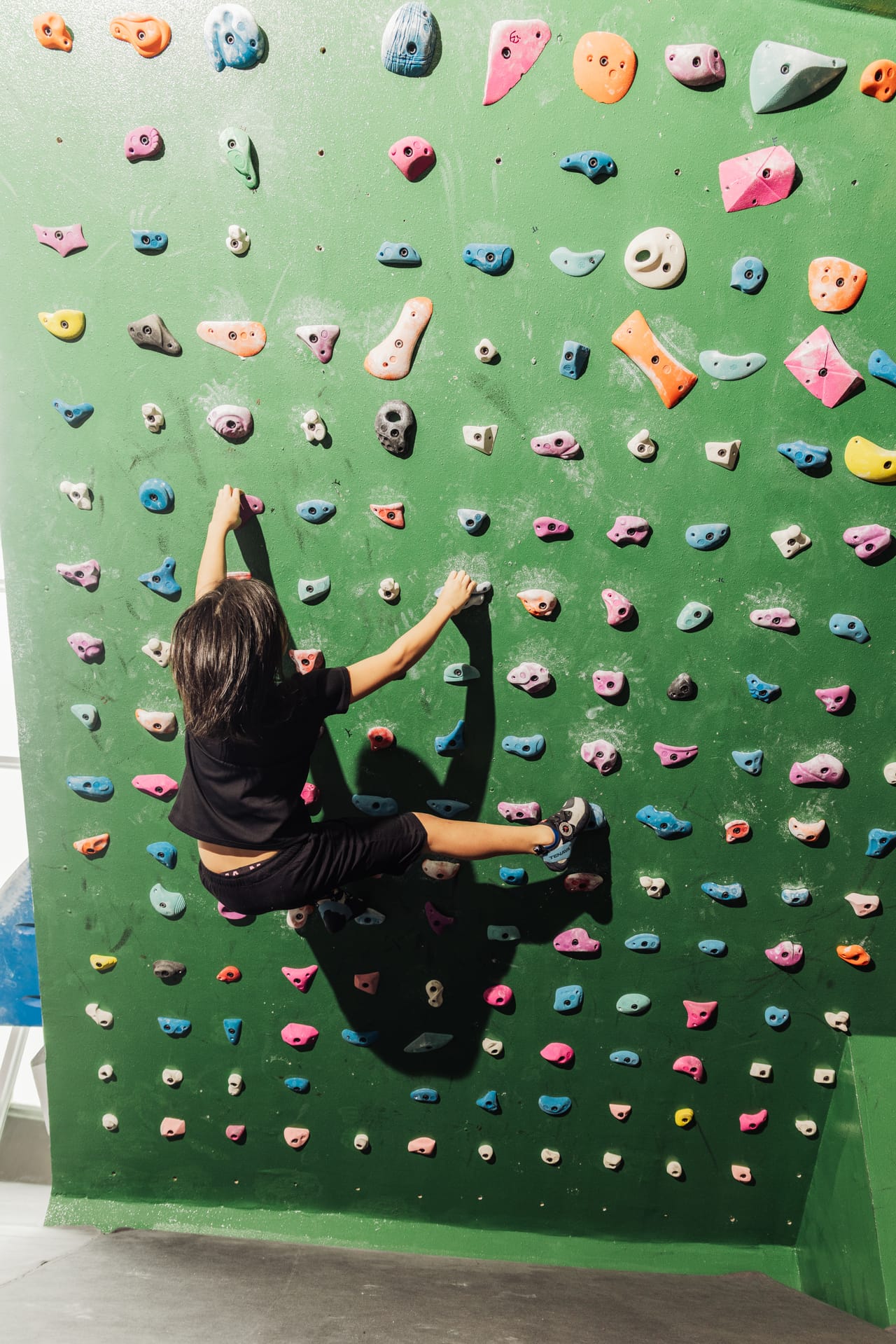 A climber trains on Climb Anytime's green system wall with its dense grid of holds
