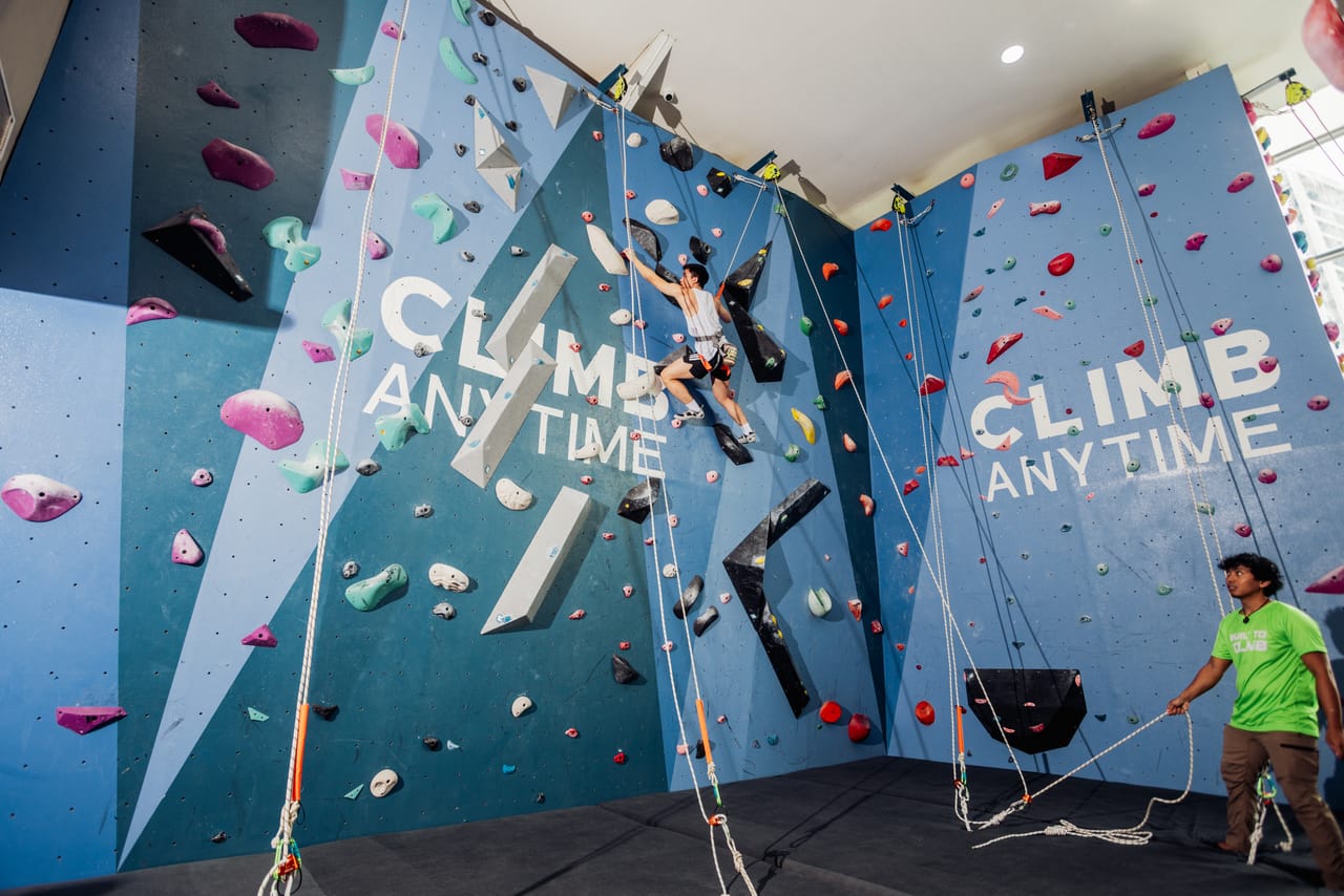 A staff belayer keeps a top-rope climber safe on Climb Anytime's branded blue walls